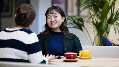 image of two female students sat at a table talking, one with her back to the camera