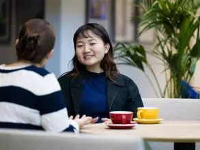 image of two female students sat at a table talking, one with her back to the camera