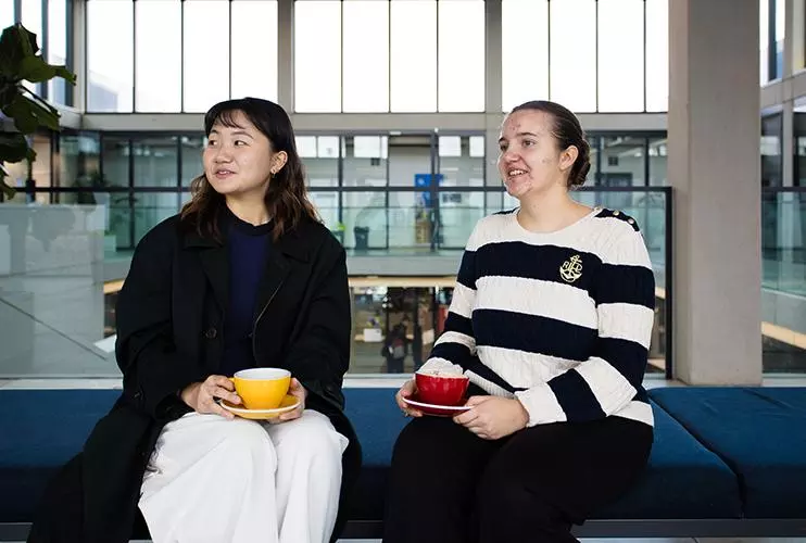 image of two students sat down on a bench facing the camera